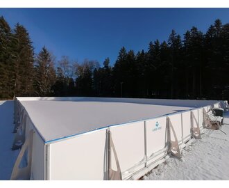 Empty ice rink with boards in the snow, surrounded by snowy forest and blue sky in Mitterberg | © Häuserl im Wald
