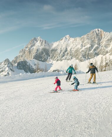 Two adults and two kids skiing in front of snowy Dachstein massif in the Austrian Alps | © Peter Burgstaller