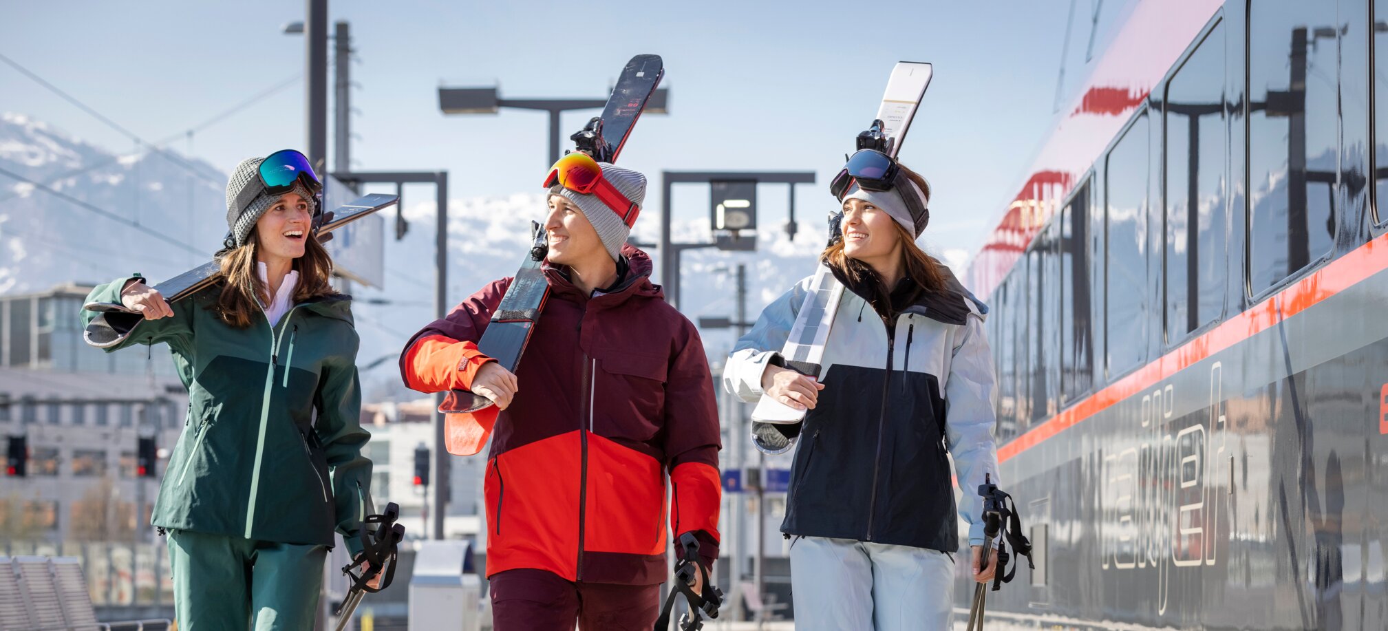 Three people with ski equipment walk along the platform next to the train | © ÖBB | Harald Eisenberger