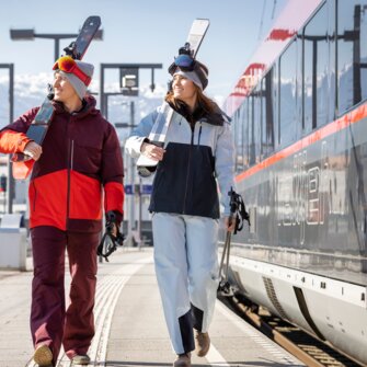 Three people with ski equipment walk along the platform next to the train | © ÖBB | Harald Eisenberger